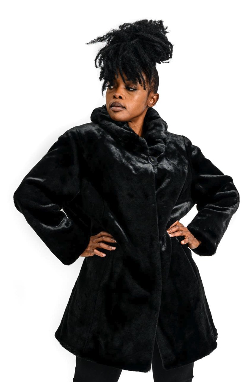 Woman wearing a black A-line faux fur jacket with draped collar and single button closure